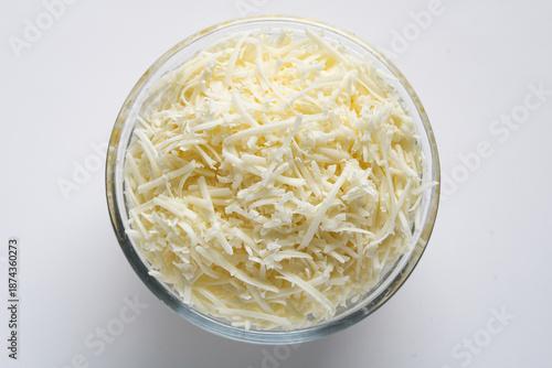 Top view of a bowl of shredded cheese displayed in a clear glass bowl on a clean white background. Ideal for food photography, cooking ingredients, and dairy product stock imagery.