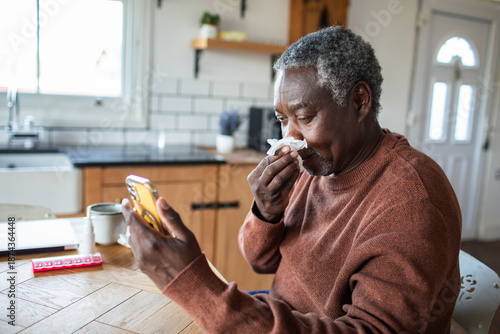Senior man feeling unwell using smartphone at home kitchen table