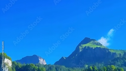 Majestic mountain peak under a clear blue sky with lush green forest landscape , Adventure, tourism, summit, sunny, rocky, wilderness, destination, background.