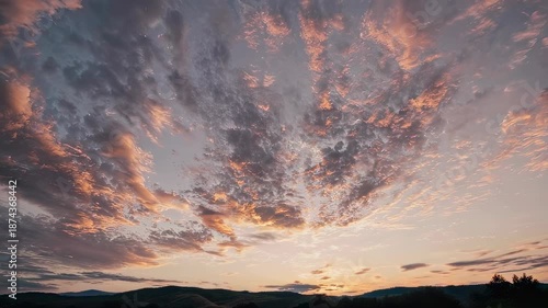 Vibrant pink and purple clouds stretch across a vast evening sky as the sun sets behind gentle rolling hills. the tranquil scene captures a perfect balance of light and shadow, evoking feelings of pea