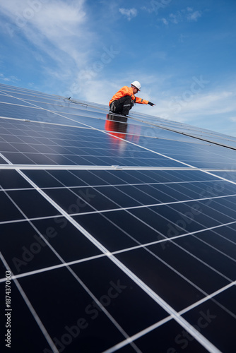 Technician installing solar panels on factory roof for green energy. A skilled technician in safety gear is working on a solar panel installation on rooftop.