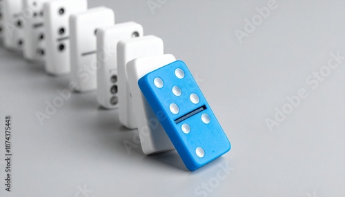 Row of white dominoes with black dots and one blue domino toppling, suggesting start of chain reaction