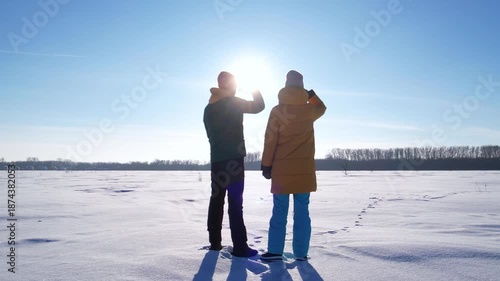 Young couple standing on a snowy field pointing at land and discussing future plans and property development. Concept of real estate, construction and planning.