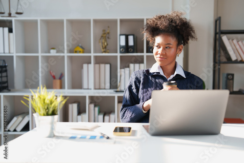 Photos Young African American lawyer researching cases on a laptop, sipping coffee and