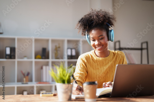 Obraz na płótnie Young Black woman with headphones studying and taking notes at a modern home off