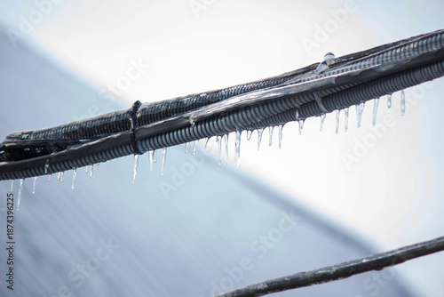 Quadro su tela Icy icicles on electric wires against blue sky, freezing rain consequences