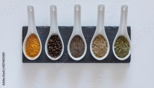 A selection of colorful spices and herbs in small white spoons on a black slate board