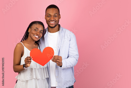 Wallpaper Mural St. Valentines Day Concept. Portrait of happy black couple in love holding red paper heart card, smiling guy embracing his woman, looking at camera, isolated on pink studio background, free copy space Torontodigital.ca