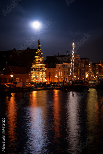 Moonlit canal with illuminated historic houses and boats at night in Leiden, Netherlands. Calm water reflections and romantic winter city atmosphere.