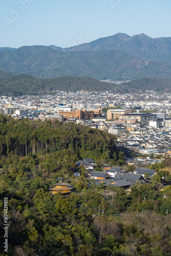 View of traditional rooftops nestled among lush green trees, contrasting with the modern cityscape and distant mountains, Kyoto, Kyoto, Japan.