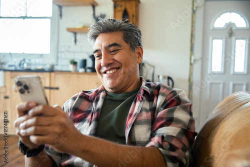 Billede på lærred Mature man smiling at smartphone on sofa at home