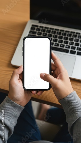 Person holding smartphone near laptop