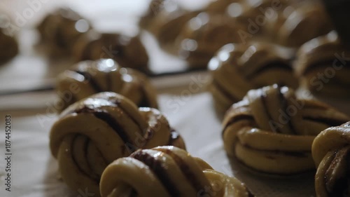 Close-up of an artisan baker brushing egg wash onto Scandinavian cinnamon and cardamom morning buns before baking. Traditional Nordic pastry process, morning pastry, natural light, hygge mood. Small  
