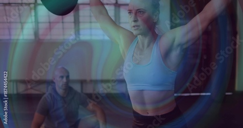Foto Lifting woman in sports bra and dark leggings pressing kettlebell overhead in gy
