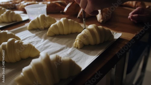 A baker brushes croissants with egg yolks before baking. Traditional process for making French croissants in an artisan bakery.