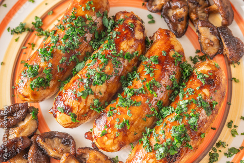 Glazed chicken sausages with herbs and mushrooms on decorative plate studio food