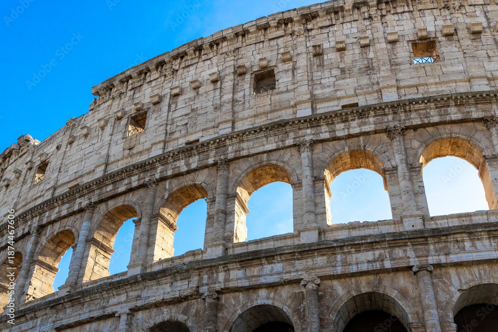 Obraz premium Famous Coliseum in Rome. Colosseum, or Coliseum. Part of the wall of an antique stone structure with arches. Italy, Europe. Famous touristic place in the world, Europe. Beautiful blue sky background.