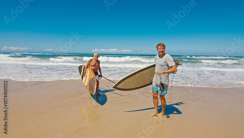 Young and elderly surfers walk with surfing boards on the beach in Brazil