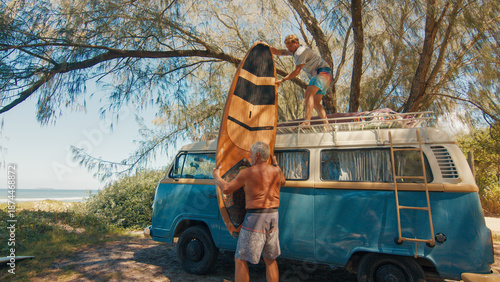 Two men unload surfing boards from the roof of the classic retro bus. Modern hippies travel by retro bus in a search of perfect waves in Brazil