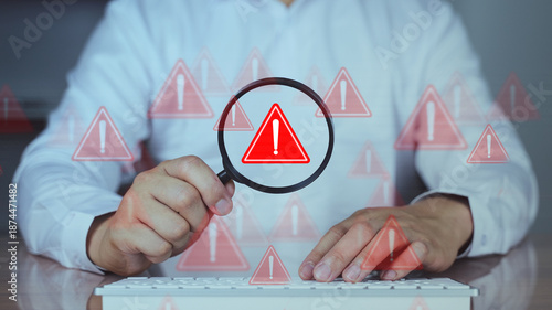 Person examining computer screen using magnifying glass with red warning symbols, representing cybersecurity risk, data breach or malware alert.
