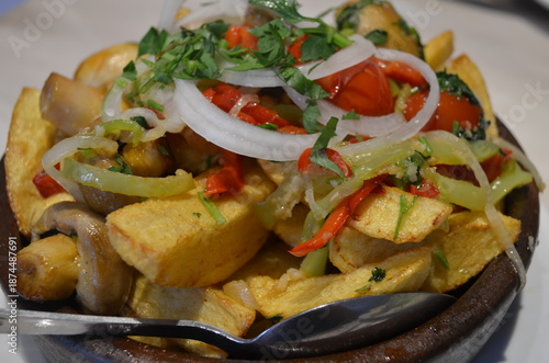 A dish of baked potatoes with vegetables on a clay plate.