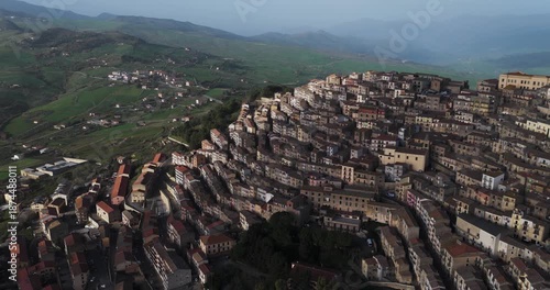 Aerial view of the tightly packed settlement of Gangi cascading down a hillside with lush green fields in the background, Gangi, Sicily, Italy.