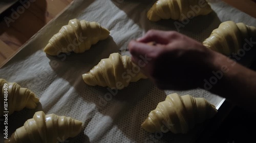A baker brushes croissants with egg yolks before baking. Traditional process for making French croissants in an artisan bakery.