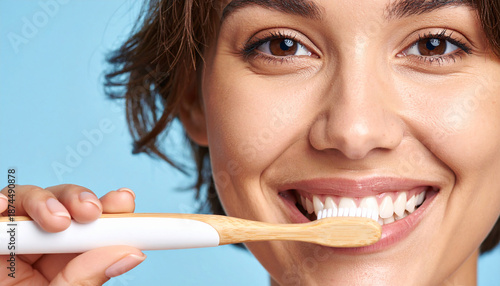 Mujer sonriendo mientras se cepilla los dientes con un cepillo ecológico en fondo azul limpio, concepto de higiene diaria, salud bucodental clínica dental y bienestar personal