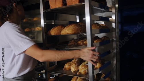Baker loading freshly baked artisan bread onto industrial metal racks and moving around bakery space. Transferring hot loaves for cooling in a professional bakery production process. Freshly baked.