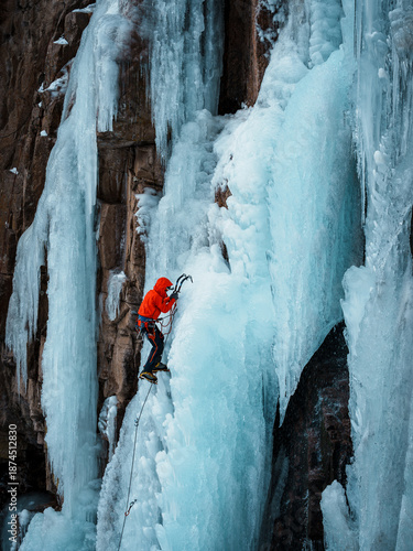 Professional ice climber ascending a steep frozen waterfall with technical gea