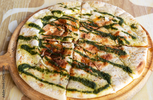 Freshly baked focaccia flatbread sliced on wooden board and drizzled with green pesto sauce. Traditional Italian bread with crispy crust, served on a rustic table. Mediterranean cuisine and bakery