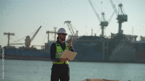 Worker inspects shipping area at port during daytime while using tablet for checks