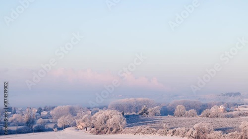 Winter rural panorama footage of a small village surrounded by frosted fields and trees, soft morning light and gentle pastel tones, peaceful seasonal scene.