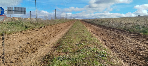 Camino rural de tierra con hierba en el centro bajo cielo azul con nubes en Burgos, España