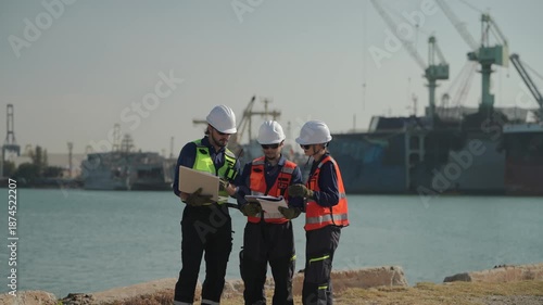 Workers discuss plans by the water at a busy port during the day