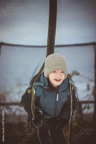 Boy playing with snow outdoors on winter day. Child enjoying winter nature, cold weather and seasonal outdoor activity.