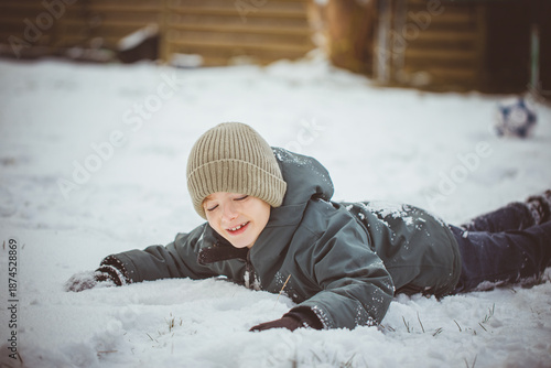 Boy playing with snow outdoors on winter day. Child enjoying winter nature, cold weather and seasonal outdoor activity.
