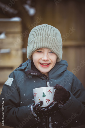 Boy drinking tea while standing on snow covered field during winter