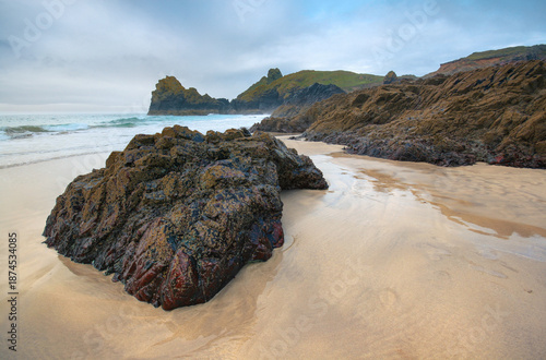 Large dark rocks on smooth sand beach at Kynance Cove, ocean in background