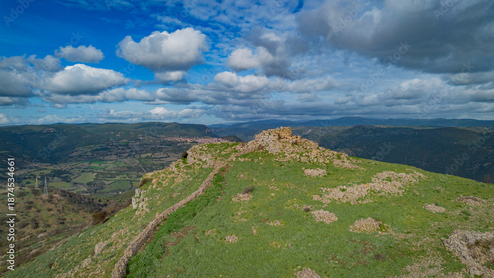 Fototapeta premium Prehistoric nuraghe stone structure rising from green landscape under dramatic sky in Sardinia