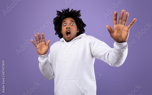 Shocked black teen guy making protection gesture, feeling frightened on violet studio background, panorama. Terrified African American adolescent expressing emotion of fear