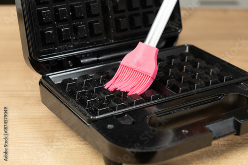 Preparing a black electric waffle maker with oil for baking.