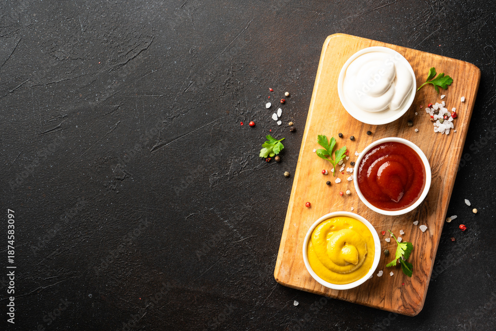 Fototapeta premium Ketchup, mayonnaise and mustard in the bowls on black background.