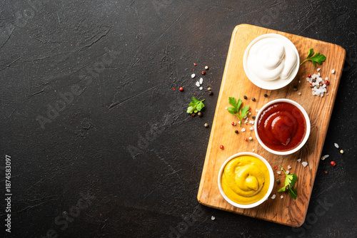 Ketchup, mayonnaise and mustard in the bowls on black background. © nadianb