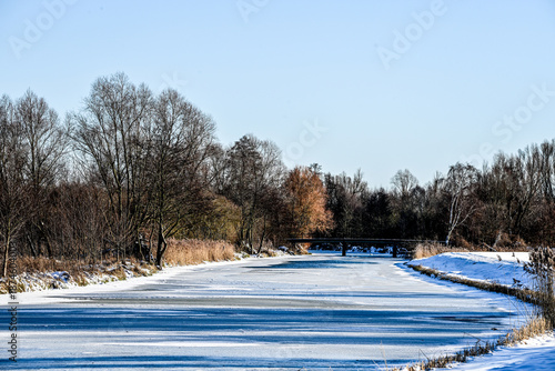 Winter scenery in the Spreewald region, Brandenburg, Germany, on a bright sunny day: snow-covered meadows and riverbanks along the River Spree and its canals, frozen waterways under a clear blue sky, 