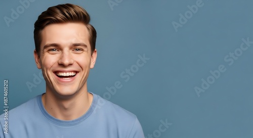 Smiling young man with brown hair and blue shirt against a blue background.