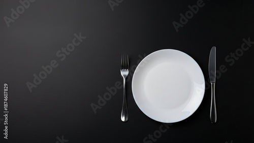 White dinner plate with fork and knife on a dark background for restaurant menu, dinner invitation, or food blog. Minimalist empty setting for eating.