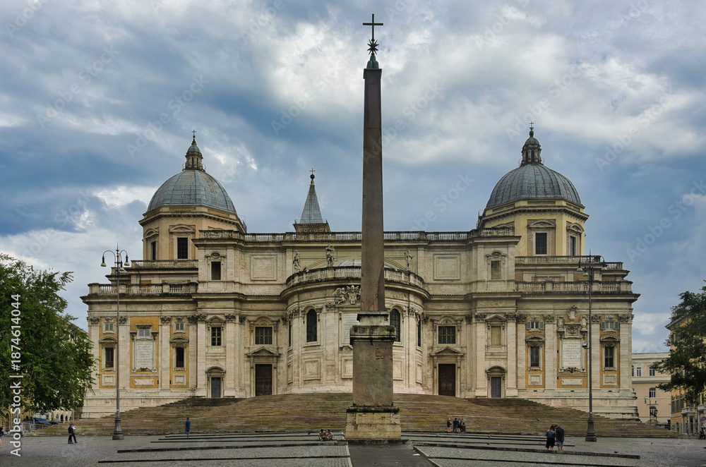 Naklejka premium View of the baroque facade of Santa Maria Maggiore papal basilica with ancient Egyptian obelisk on Piazza dell'Esquilino under dramatic cloudy summer sky