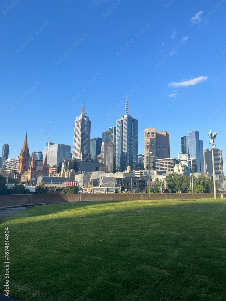 Obraz premium Melbourne skyline with skyscrapers and green park lawn under a clear blue sky