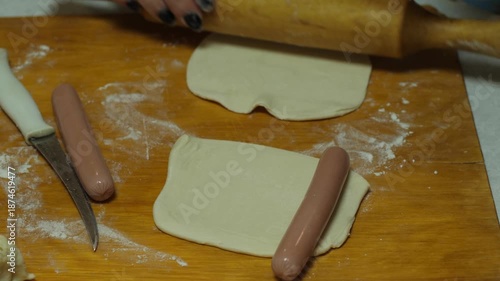 Close-up female chef hands rolling dough wrapping sausages preparation process.